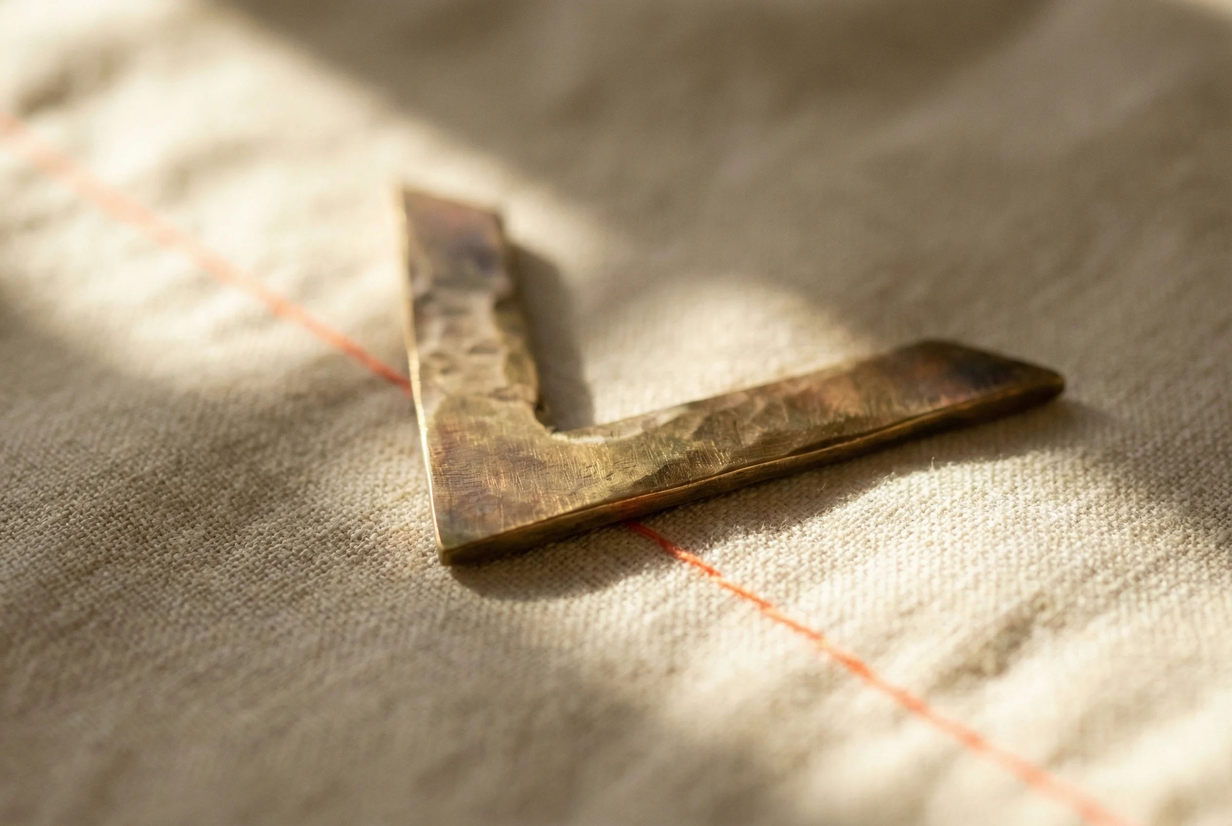 Hand-hammered brass chevron on linen — brand motif